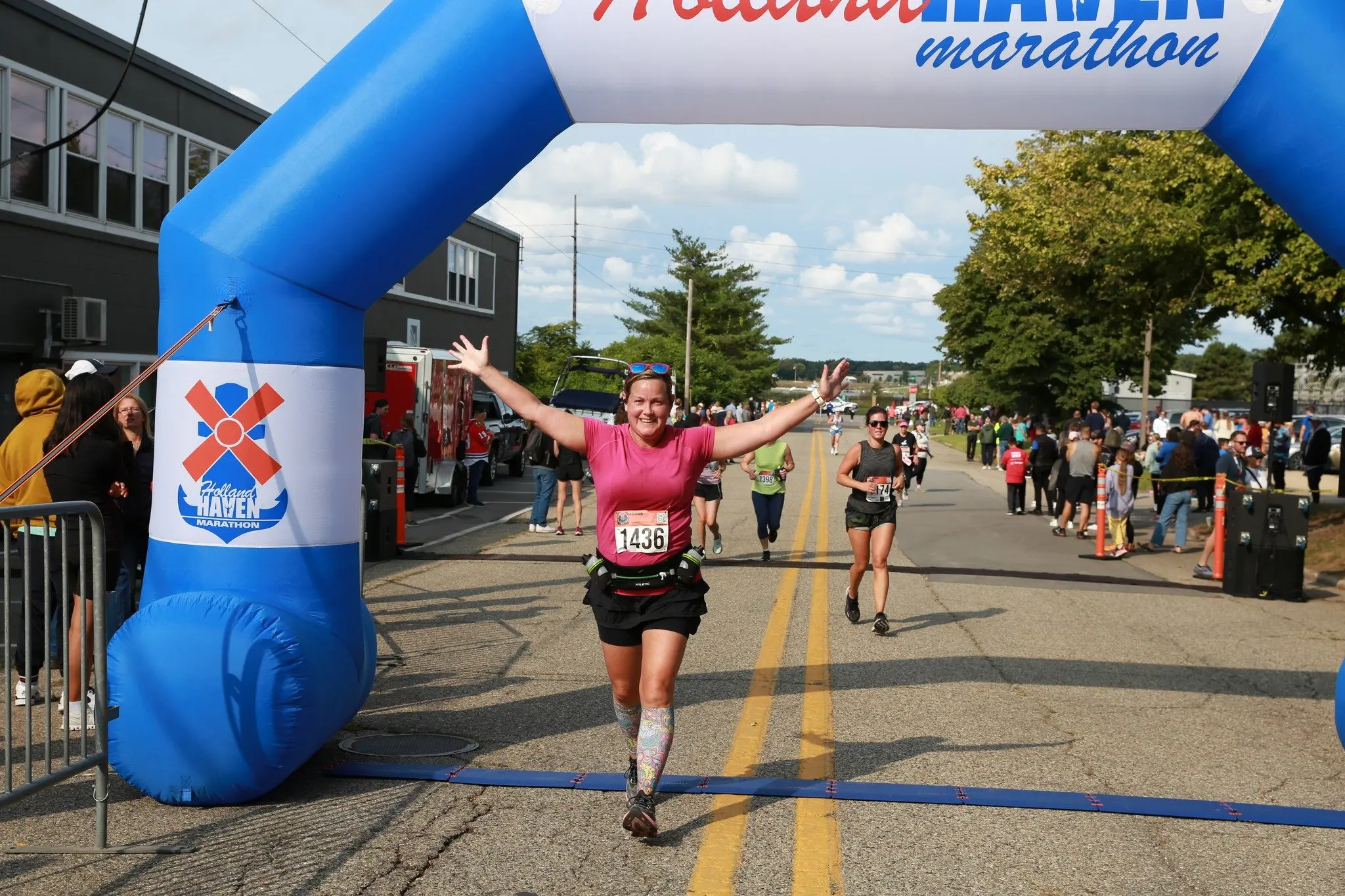 A smiling Holland Haven runner celebrates crossing the finish line beneath the blue race arch